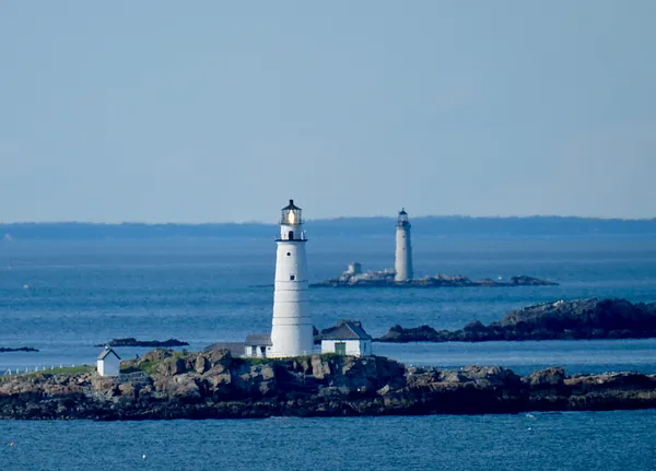 A white lighthouse on a rocky island with a smaller lighthouse visible farther out across calm blue water.